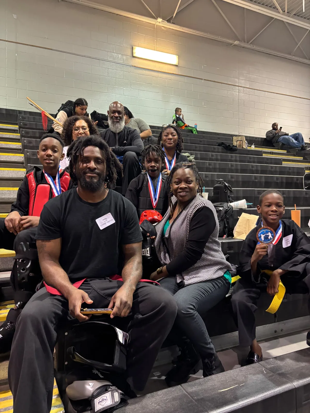 Young martial artists wearing medals seated with adults at an event